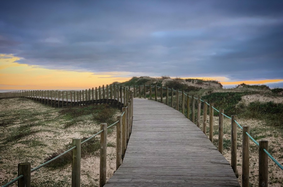 A wooden boardwalk crossing a marram-grass dune down to the beach at sunset