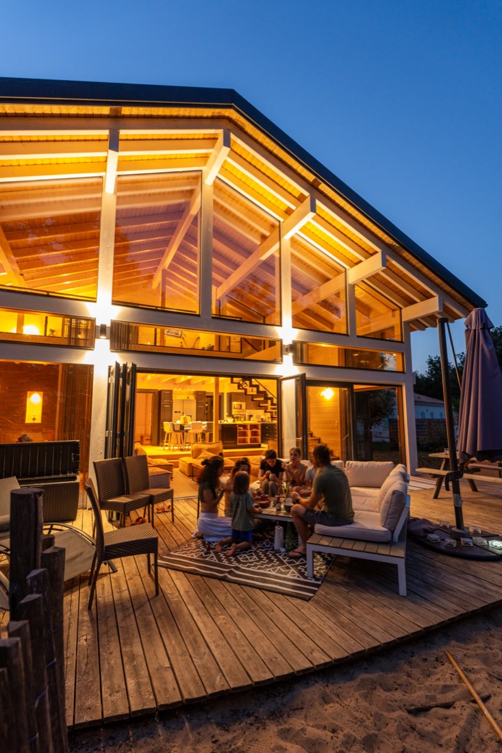 Soirée sur la terrasse du Chalet Moana, façade vitrée illuminée et convives attablés à la tombée du jour