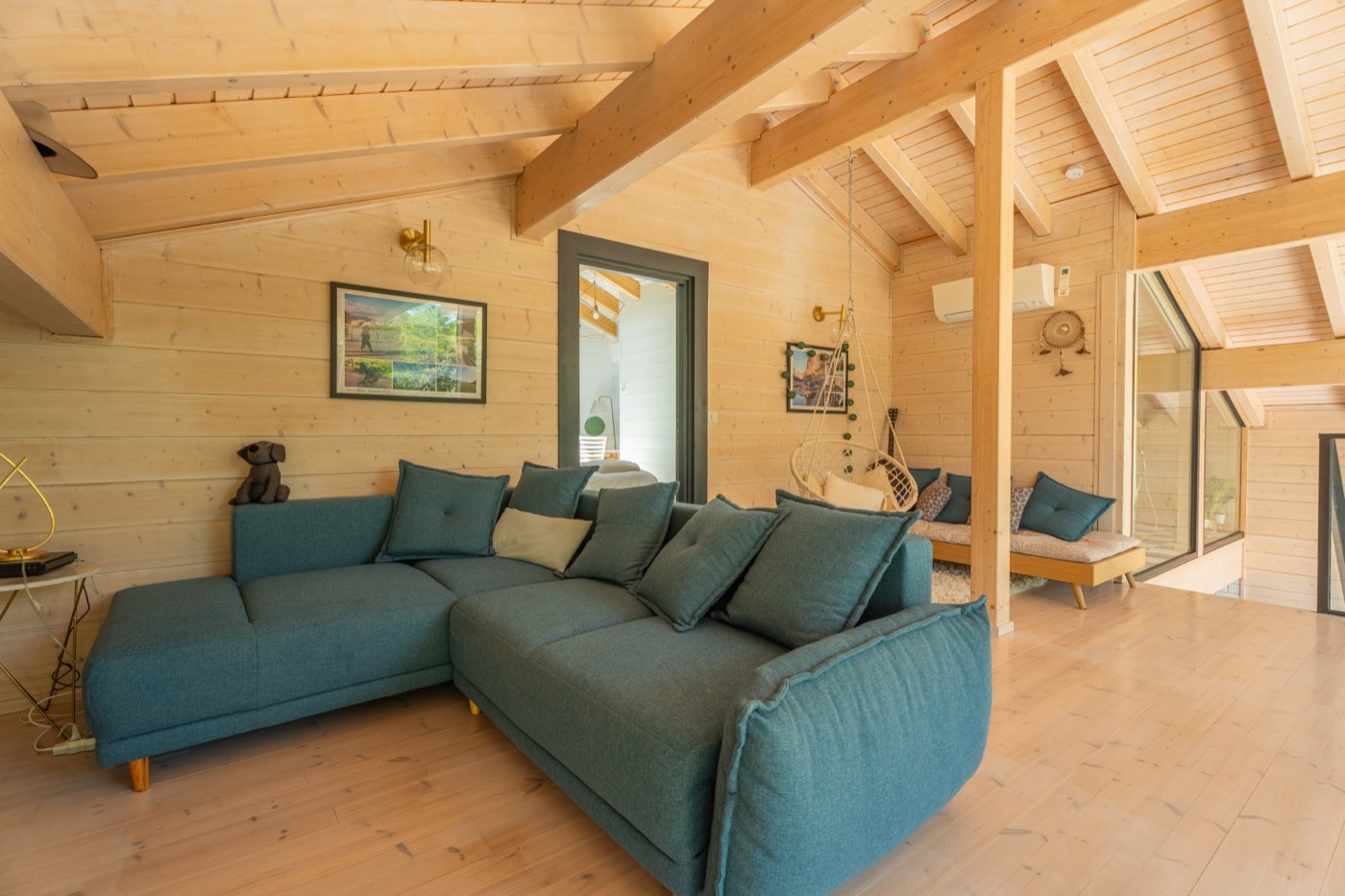 Mezzanine ouverte du Chalet Moana avec grand canapé bleu, fauteuil suspendu et vue plongeante sur la pièce de vie